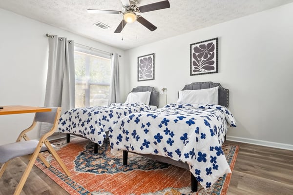 Twin bedroom with blue floral bedding, grey upholstered headboards, and a wooden desk